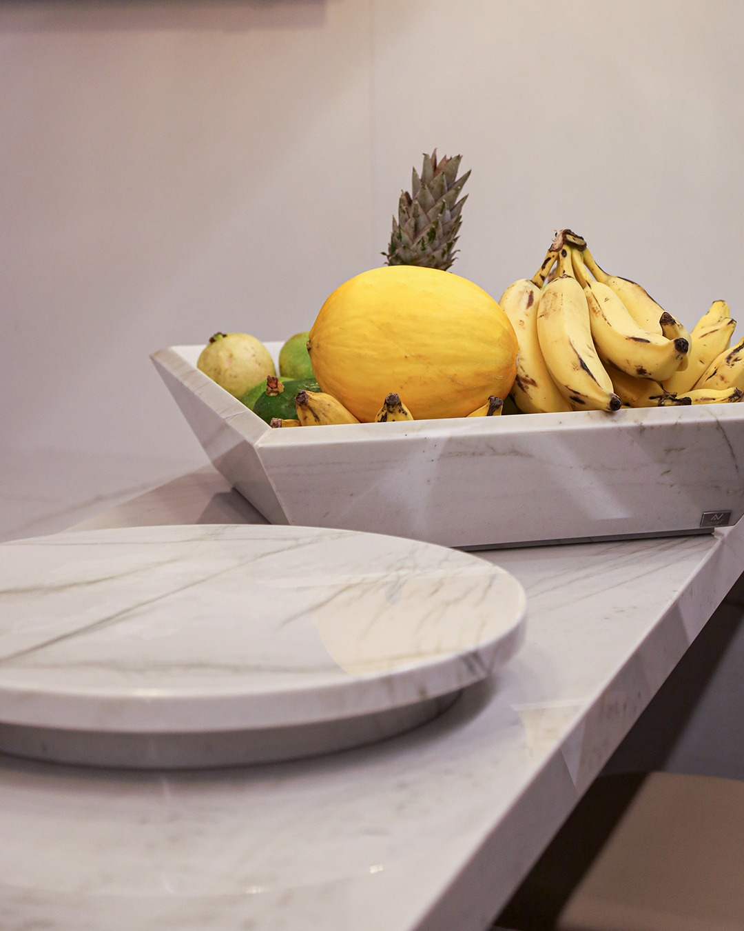 Fruteira em rocha natural sobre bancada, ao lado de bandeja redonda em mármore